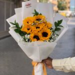 Bouquet of Sunshine with 10 sunflowers, gypsophila, and seasonal fillers wrapped in white paper and yellow ribbon