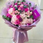 Vibrant floral bouquet with pink hydrangeas, fuchsia roses, and pink carnations wrapped in purple paper