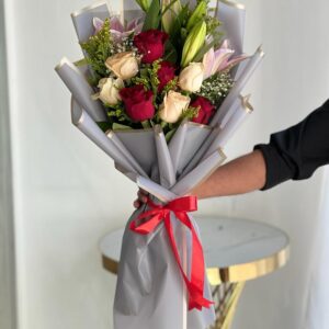 My Cutie Pie bouquet with red and peach roses, pink lily, and seasonal fillers wrapped in grey paper