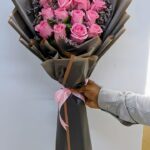 Pink Blushing bouquet with 16 pink roses, limonium, and seasonal filler wrapped in brown paper with pink ribbon